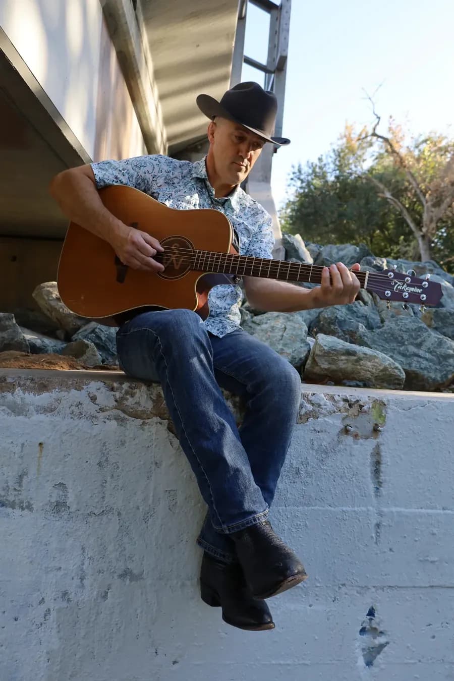 Shawn Wrangler seated outdoors with his guitar